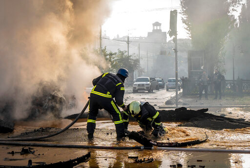 A firefighter helps his colleague to escape from a crater as they extinguish smoke from a burned car after a Russian attack in Kyiv, Ukraine, Monday, Oct. 10, 2022. Russia unleashed a lethal barrage of strikes against multiple Ukrainian cities Monday, smashing civilian targets including downtown Kyiv where at least six people were killed amid burnt-out cars and shattered buildings. The onslaught brought back into focus the grim reality of war after months of easing tensions in the capital. (AP Photo/Roman Hrytsyna)