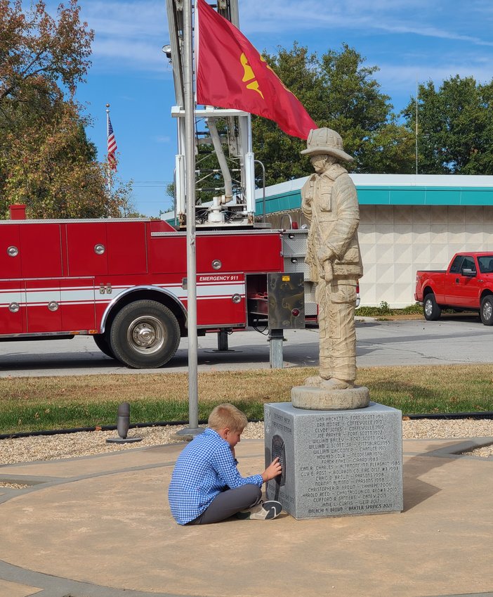 Colton Hunt sits in front of the newly modified memorial after the 35th Annual Fallen Firefighters Memorial Service in Girard on Sunday.
