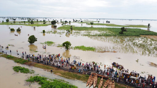FILE - People walk through floodwaters with flooded farmlands forground after heavy rainfall in Hadeja, Nigeria, Sept 19, 2022. West and Central African countries are battling deadly floods that have upended lives and livelihoods, raising fears of further disruption of food supplies in many areas battling armed conflict. &ldquo;Above-average rainfall and devastating flooding&rdquo; have affected 5 million people this year in 19 countries across West and Central Africa, according to a new U.N. World Food Program situation report. (AP Photo, file)