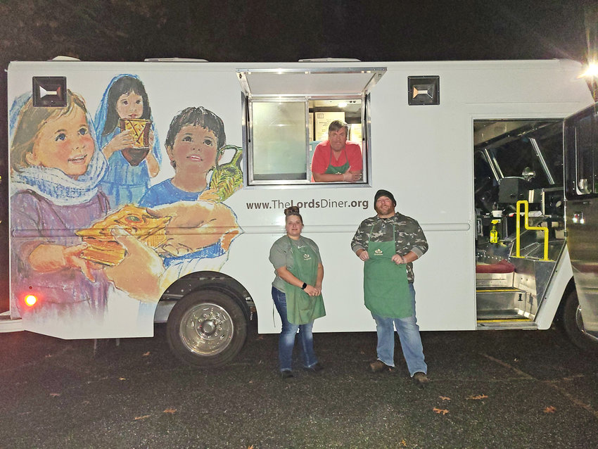Volunteer Steve Wolfe peeks out of the window of The Lord&rsquo;s Diner food truck with Volunteer Coordinator Anna Oberle, left, and volunteer Matthew Circle on Thursday evening at Deramus Park.