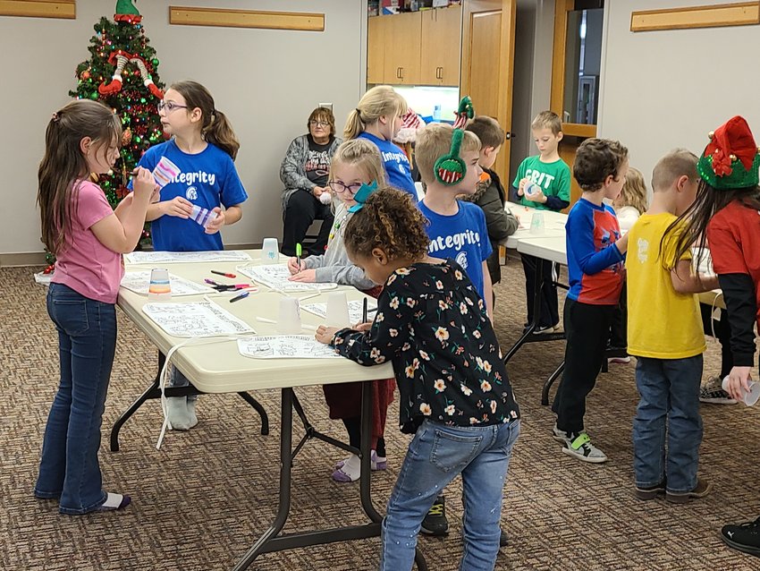 Children color aprons and plastic cups to melt for ornaments during the Girard Public Library children&rsquo;s Christmas party on Wednesday afternoon.