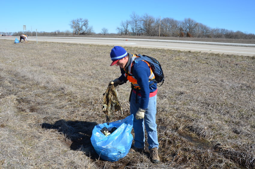 Matt Van Becelaere picks up plastic and trash in the mud along Highway 69 north of 680th Avenue on Friday afternoon.