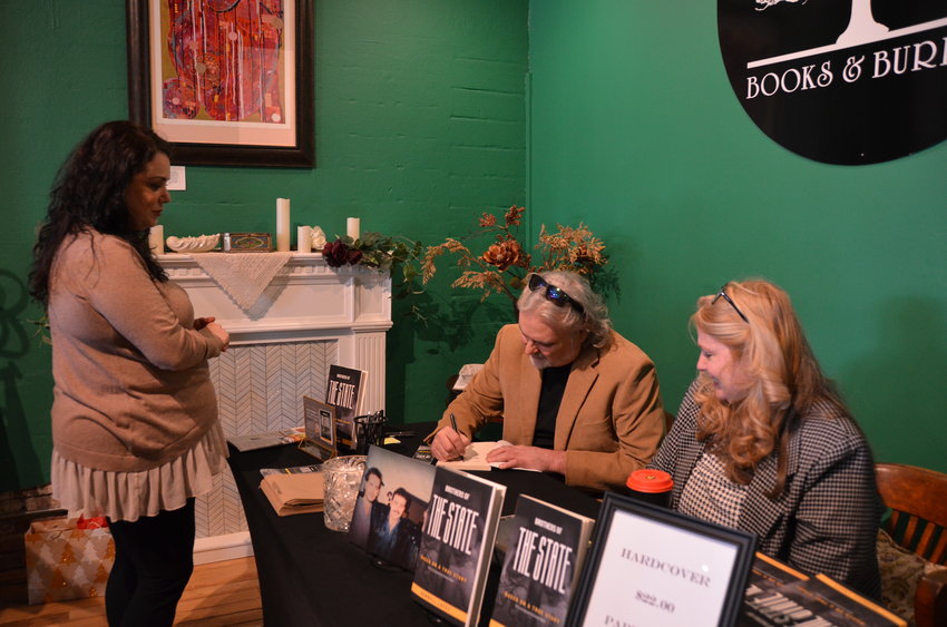 From left, Maria McDonald gets a book, &ldquo;Brothers of the State,&rdquo; signed by Darrell Lacey during his &ldquo;meet the author&rdquo; event with the support of Karla Highfill at Books and Burrow on Saturday afternoon. Lacey&rsquo;s book tells the story of three brothers who were taken into a foster home and the horrors they experienced.