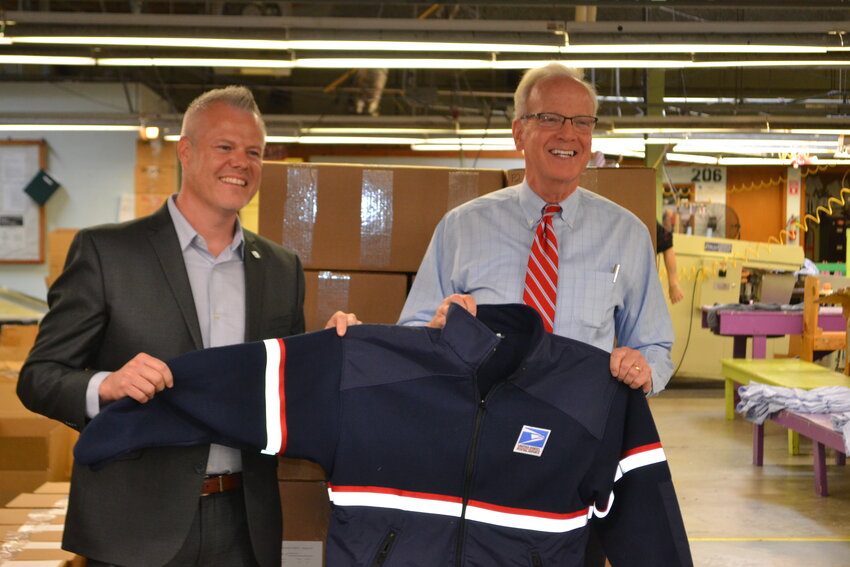 Senator Jerry Moran (R-Kan.) and Markin Dornan, vice-president of NSA Military, holds up a United State Postal Service jacket made at National Safety Apparel in Baxter Springs. Senator Moran was nearing the end of a tour through Kansas, having already visited Coffeyville, Parsons, and Wichita.