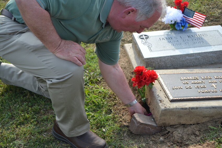 Retired Air Force Colonel Jim Kuhns places sand from Omaha and Utah Beaches under his father&rsquo;s headstone. Lt. James Kuhns was a glider pilot during the Normandy and Holland invasions in 1944.