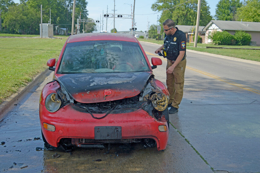 Officer Chris Kmiec with the Pittsburg Police Department inspects a red Volkswagen Beetle that had caught fire and was left abandoned at the intersection of S. Joplin Street and E. Jefferson Street shortly after 5 p.m. Friday, June 16.
