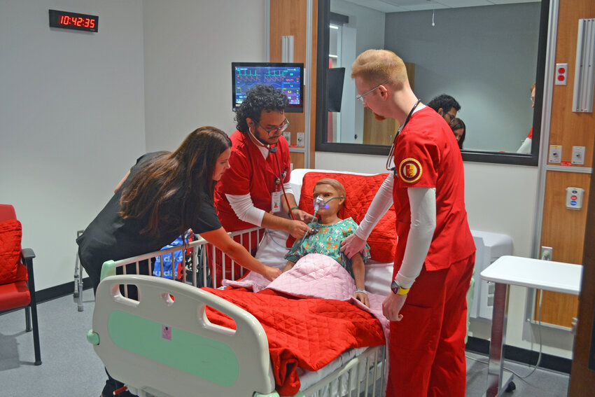 Nursing students, in red, under the supervision of an instructor, monitor the condition of one of the hospital&rsquo;s &ldquo;patients.&rdquo; Each room in the hospital is designed for a different simulated experience with a variety of patients.