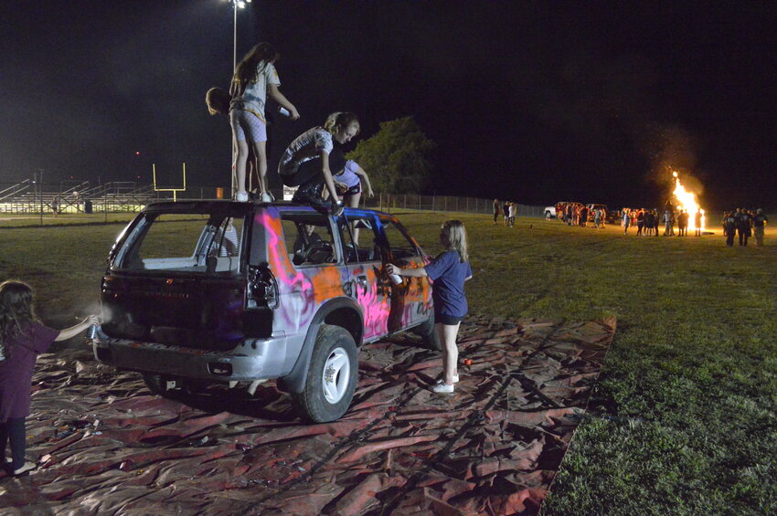 Northeast students spray paint a car donated by Chris Lewellen while other students gathered around a bonfire Wednesday night at Northeast High School. The event followed a homecoming pep rally, Iron-Man competition and powderpuff football game.