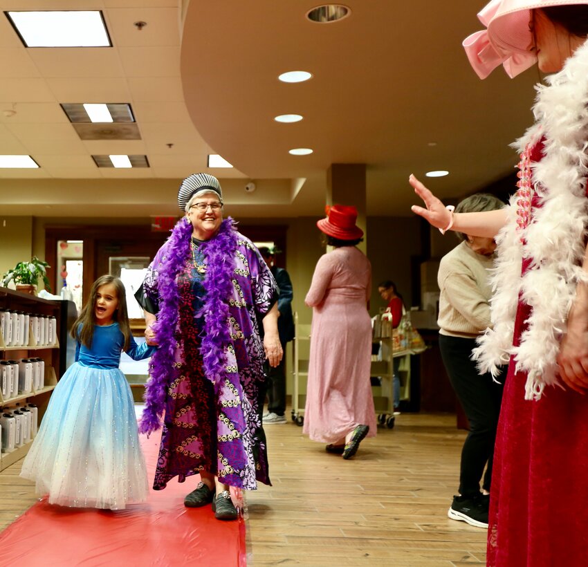 Pittsburg Public Library Youth Services Librarian Gail Sheppard walks a young princess down the red-carpet during Tuesday&rsquo;s Valentine Tea Party. Throughout the evening, after walking down the carpet in their best prince and princess attire, area children had the opportunity to take fancy pictures before venturing into the children&rsquo;s library section for a puppet show and dance party. Attendees also made their way into the library&rsquo;s conference room for treats and valentine's activities.