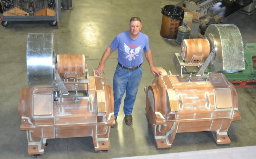 Pattern maker Jim VanBeceleare stands between the two wooden replica motors he built for the Big Brutus Museum. VanBeceleare was hired by the museum to replicate the massive engines as part of restoration efforts. The motors will be installed in the massive machine once painting is completed. Until then, the motors will be on display in the museum once they receive their coat of pea-green paint.