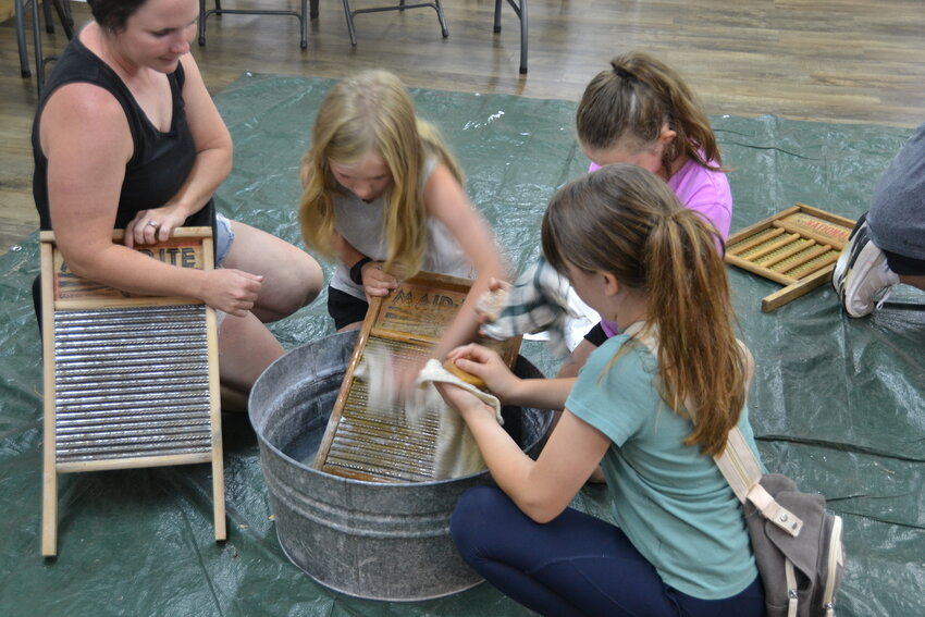 Visitors try their hand at laundry day using lye soap and washer boards. After it has all been washed and dried, the laundry then had to be pressed using an iron heated in a fire.