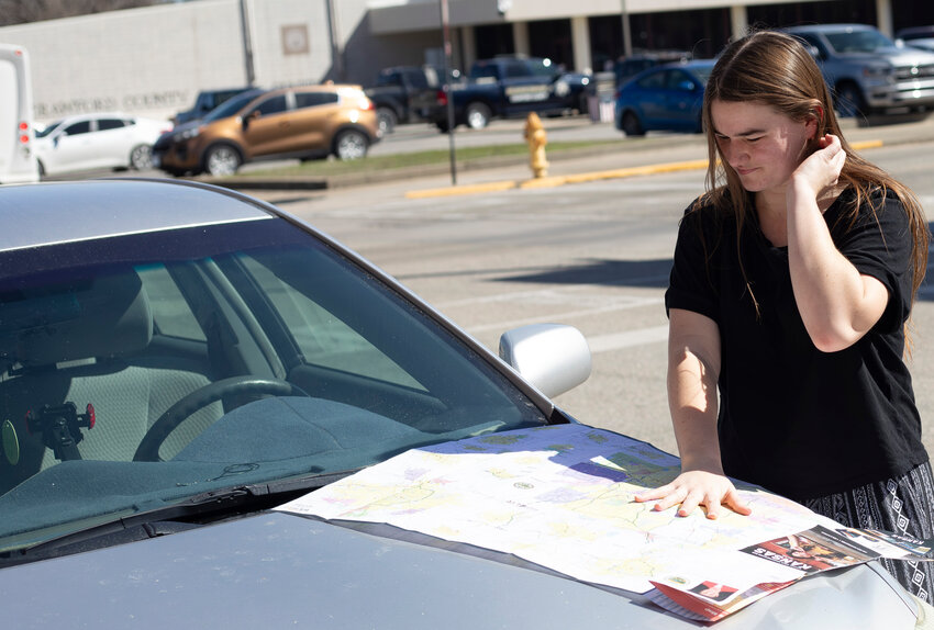 Amber Ross looks at the 2023-2024 Kansas State Transportation map on the hood of a car March 12.