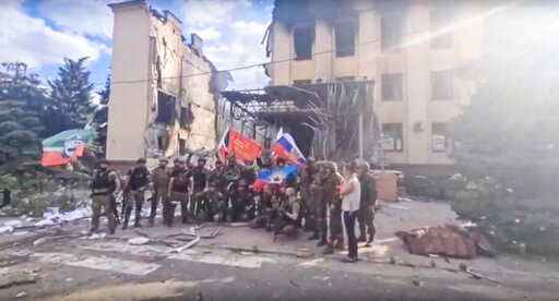 FILE - This photo taken from video provided by Ramzan Kadyrov's Official Telegram channel released on Saturday, July 2, 2022, shows Russian troops including soldiers of Chechen regiment waving Russian and Chechen republic national flags as they pose for a photo in front of a destroyed building in Lysychansk, Ukraine. After more than four months of ferocious fighting, Russia claimed full control over one of the two provinces in Ukraine’s eastern industrial heartland. (Ramzan Kadyrov's Official Telegram channel via AP, File)