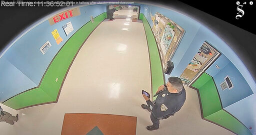 In this photo taken from surveillance video provided by the Uvalde Consolidated Independent School District via the Austin American-Statesman, shows officer Ruben Ruiz, whose wife, Eva Mireles was killed in the shooting, checking his phone in the hallway at Robb Elementary School in Uvalde, Texas, Tuesday, May 24, 2022. (Uvalde Consolidated Independent School District/Austin American-Statesman via AP)/
