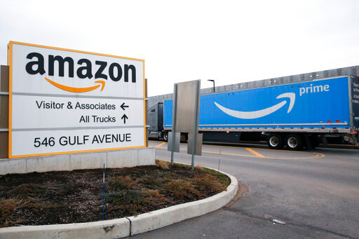 FILE - An Amazon Prime truck passes by a sign outside an Amazon fulfillment center on the Staten Island borough of New York, on March 19, 2020. Amazon is raising charges on third-party sellers again — this time adding a holiday fee for merchants who use the company’s fulfillment services to pack and ship items to customer, according to a notice the company sent to merchants on Tuesday, Aug. 16, 2022. (AP Photo/Kathy Willens, File)