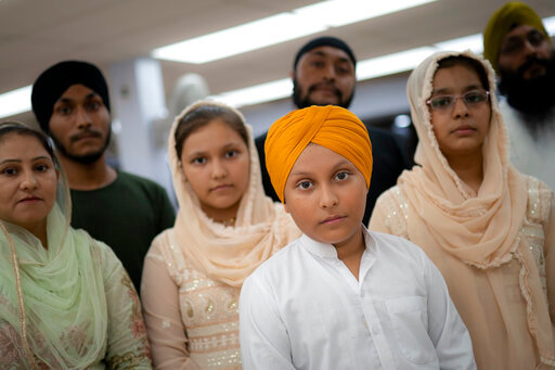 Amandeep Singh, 12, stands with his family in the communal room where "langar," food served after temple services, is provided at Guru Nanak Darbar of Long Island, a Sikh gurdwara, Wednesday, Aug. 24, 2022, in Hicksville, N.Y. Their Afghan Sikh family of 13 has found refuge in the diaspora community on Long Island where the Sikh community is helping family members obtain work permits, housing, healthcare and find schools for the children. (AP Photo/John Minchillo)