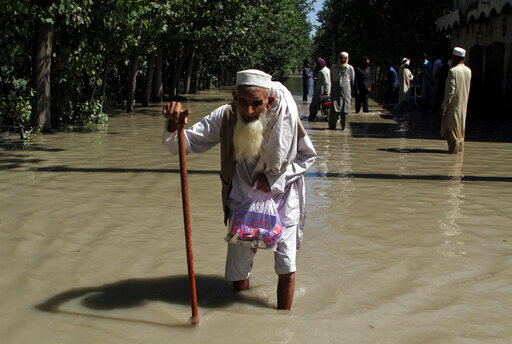 FILE - A displaced man wades through a flooded area after fleeing his flood-hit home, on the outskirts of Peshawar, Pakistan, Aug. 28, 2022. The flooding has all the hallmarks of a catastrophe juiced by climate change, but it is too early to formally assign blame to global warming, several scientists tell The Associated Press. (AP Photo/Mohammad Sajjad, File)