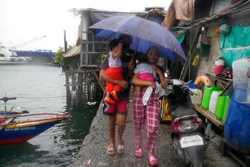 Residents carry their children as they evacuate to safer grounds to prepare for the coming of Typhoon Noru at the seaside slum district of Tondo in Manila, Philippines, Sunday, Sept. 25, 2022. The powerful typhoon shifted and abruptly gained strength in an "explosive intensification" Sunday as it blew closer to the northeastern Philippines, prompting evacuations from high-risk villages and even the capital, which could be sideswiped by the storm, officials said. (AP Photo/Aaron Favila)