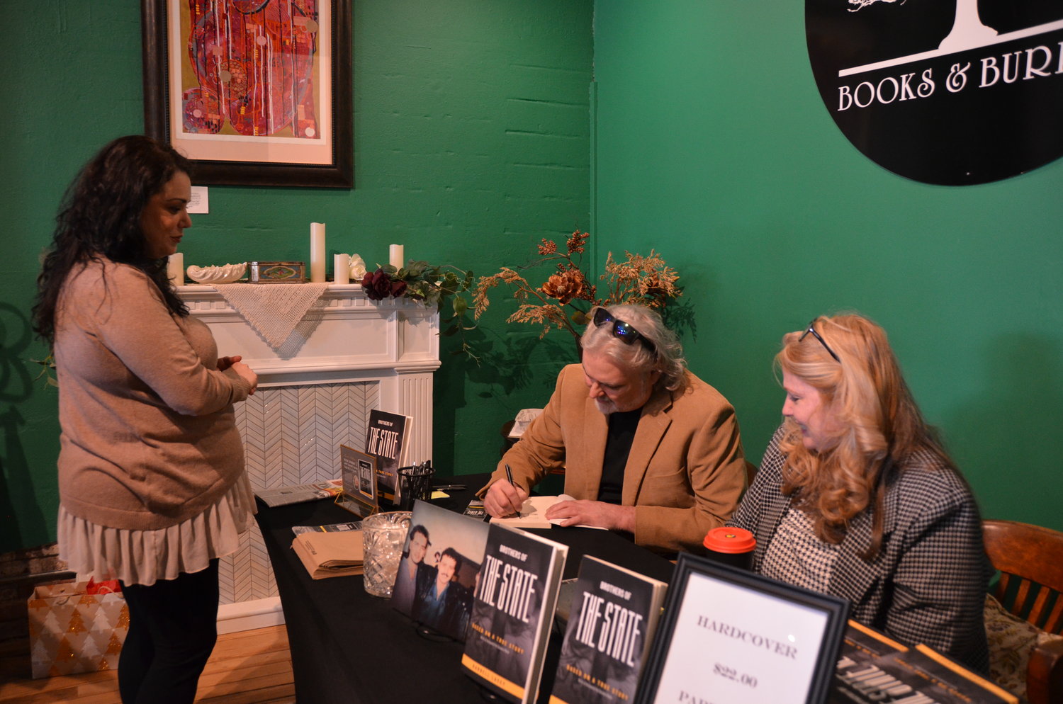 From left, Maria McDonald gets a book, “Brothers of the State,” signed by Darrell Lacey during his “meet the author” event with the support of Karla Highfill at Books and Burrow on Saturday afternoon. Lacey’s book tells the story of three brothers who were taken into a foster home and the horrors they experienced.