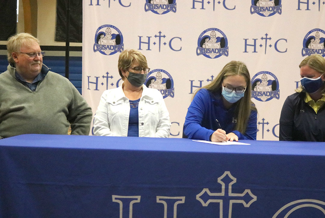 HTC senior Ali Robu signs her national letter of intent to play golf at Mt. Mercy University in Cedar Rapids Tuesday at Holy Trinity with her parents, right and new coach on the left. Photo by Chuck Vandenberg/PCC