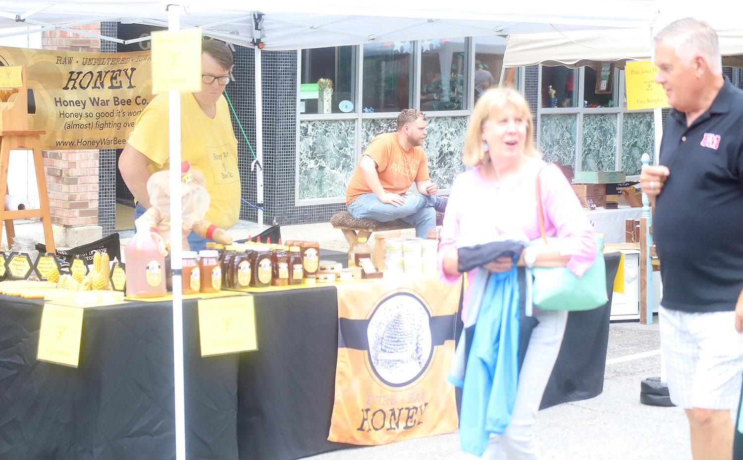 Downtown Summer Market visitors in Fort Madison stop to consider the offerings of the Honey War Bee Co.'s honey and other wares Thursday night in Fort Madison.
