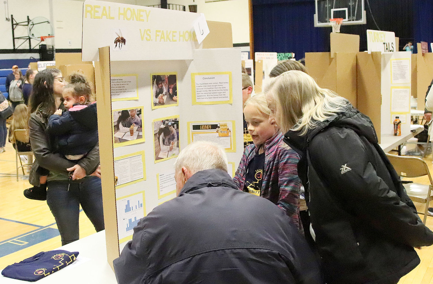 Two visitors to the Holy Trinity Catholic Science Fair in West Point Wednesday night hear about the benefits of farm-produced honey compared to retail-produced honey as told by Malani Roach, Anna Rempe, and Grayson Rhoades.