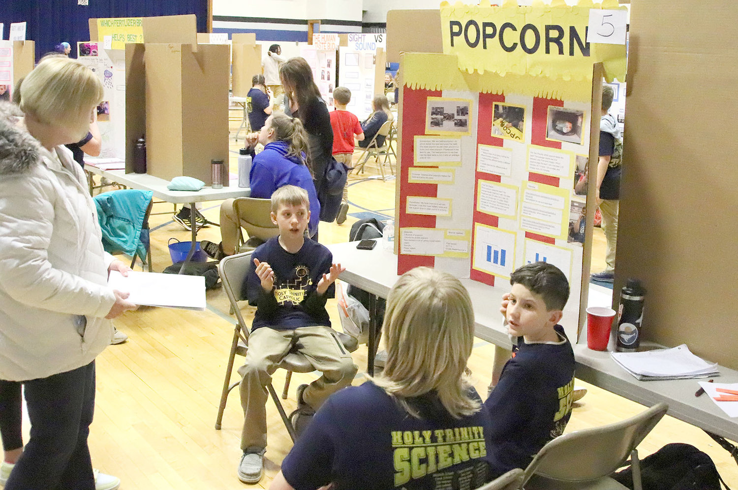 Nolan Peitz, Cooper Barnes, and Reid Schmitt talk about popcorn with a visitor who stopped by their science fair project display Wednesday night in West Point.