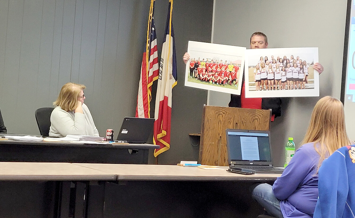Keith Gehling, a father of a Holy Trinity student participating in Fort Madison sports, holds up pictures of the Bloodhound boys' and girls' soccer teams, both shared programs with Holy Trinity Catholic. The board voted to let all current agreements with the school expire at the end of the current athletic season.