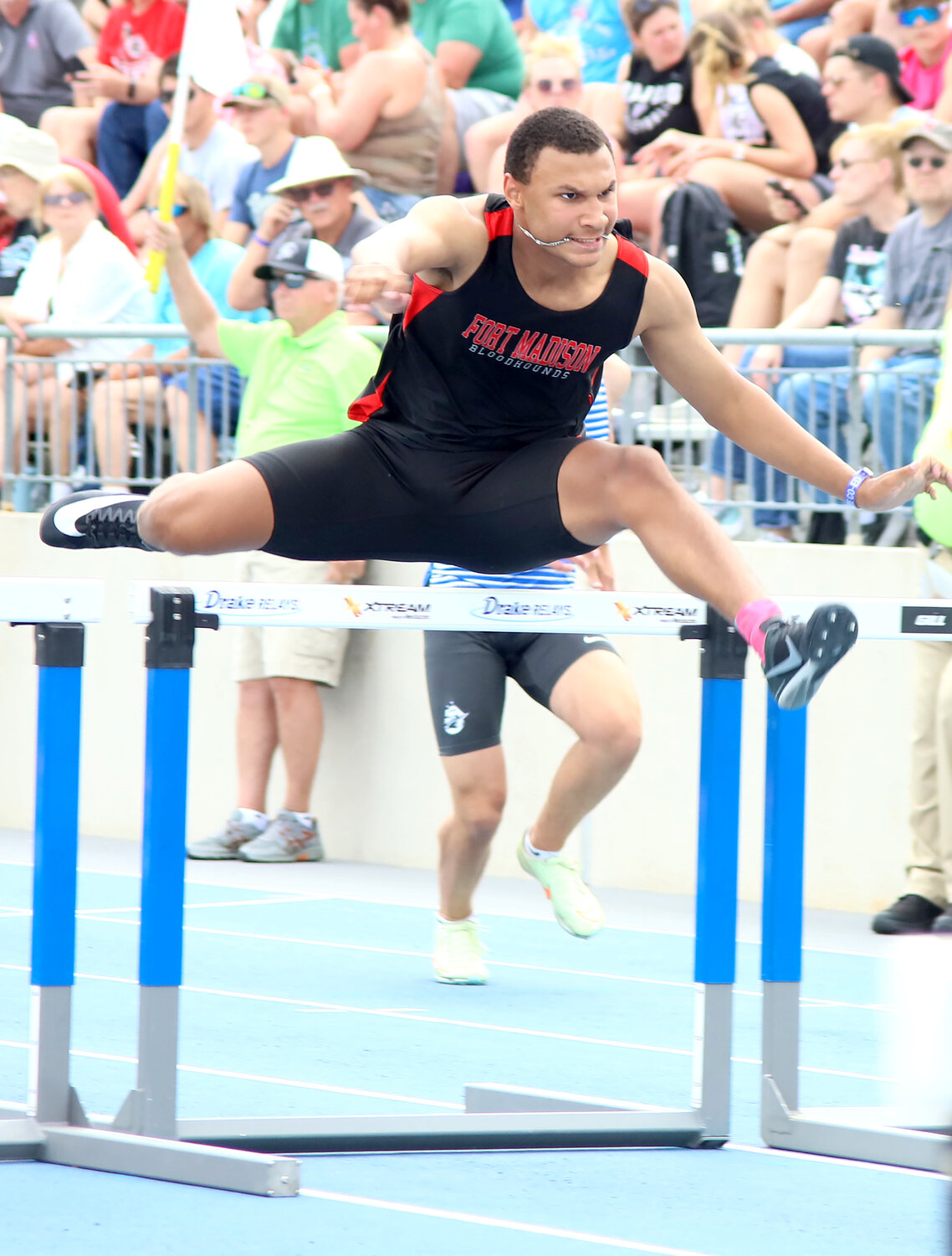 The Hounds' Kiawante Smith holds his chain in his mouth as he clears the second hurdle on the third leg of the Shuttle Hurdle Relay Thursday afternoon.