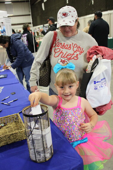 Kynlee Feldman, 5, puts her name in the bucket for a drawing at the ACC booth during Spring Fling as her mom, Mandy Feldman, looks on.  Kynlee was also part of a dancing group that entertained at the event.