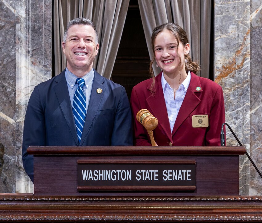 Alaina Cecil joins Sen. Brad Hawkins at the lectern in the Washington State Senate chamber. Her time as a Senate Page included interactions with state leaders, contributing to her firsthand understanding of the legislative process.