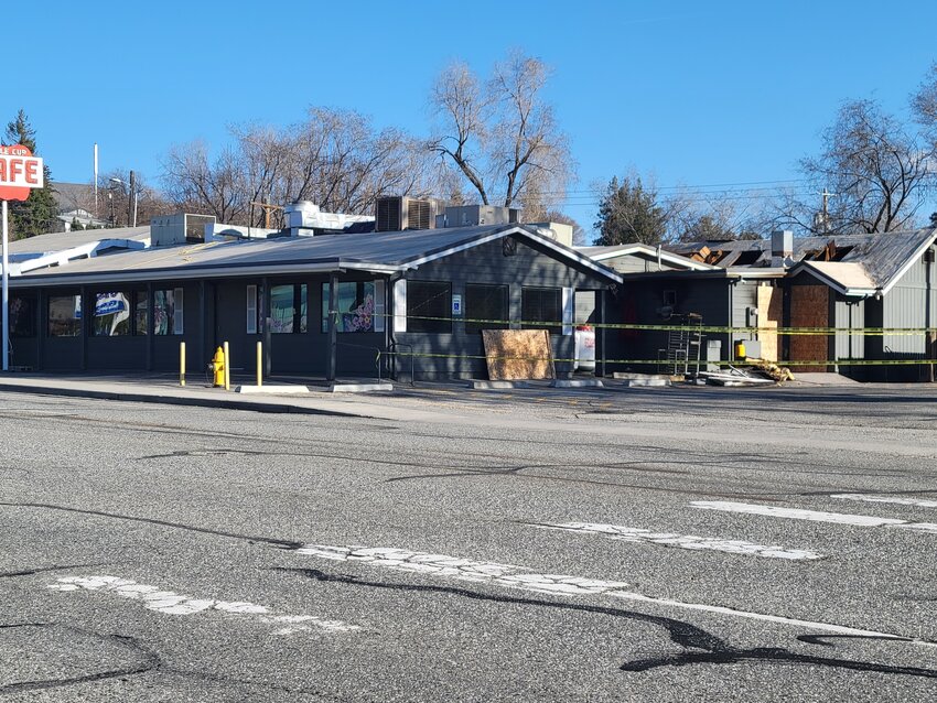 The aftermath of the fire that struck The Apple Cup Café is visible, with extensive damage to the building. Yellow caution tape surrounds the scene hours after the blaze was extinguished by firefighters