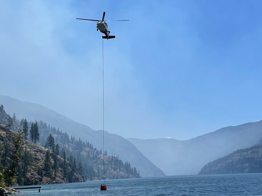 A helicopter utilizes a water bucket to conduct strategic water drops along the shore of Lake Chelan in an effort to slow the spread of the Pioneer Fire.