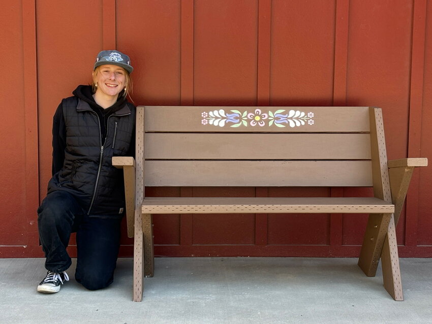 Callie Holmes kneels beside one of the four benches she constructed as part of her Eagle Scout project for the Tierra Learning Center. The wooden bench, which features decorative floral stenciling on its backrest, was built, painted and installed by Holmes with the help of friends and family. Dunn Lumber donated materials for the project.