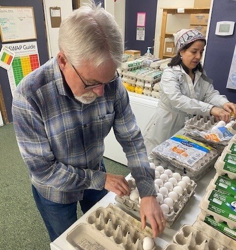 Community Cupboard volunteer Glen Ferrier and staff member Alexandra Muro repackage bulk eggs into dozen-sized cartons for individual families.