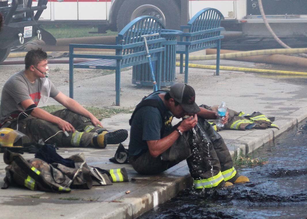 A firefighter scoops overflow water from a hydrant onto his face as he takes a break from the fire line.