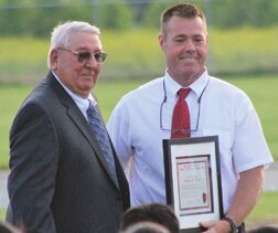 Brewster School Superintendent, Eric Driessen presents the Brewster School District Wall of Fame Inductee Certificate to Ralph J. Fries at last Friday’s outdoor graduation ceremonies on the Brewster school football field.
