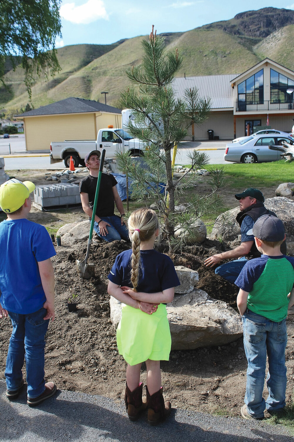 Three interested observers watch Isaac Wall, left, and Jord Wilson set a native pine in its new home at the Memorial to the Methow Park last Friday.