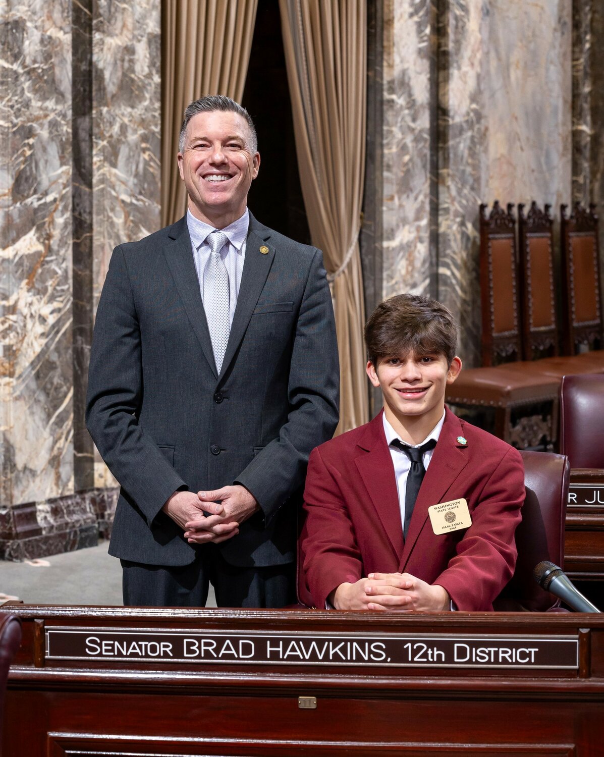 Cashmere High School sophomore Isaac Zavala (sitting) with 12th Legislative District Senator Brad Hawkins at the Capitol in Olympia, where Zavala served as a Senate page during the fourth week of the 2024 Legislative session. Isaac, who was sponsored by Senator Hawkins, gained firsthand experience in the legislative process, participating in floor voting and learning about parliamentary procedures.