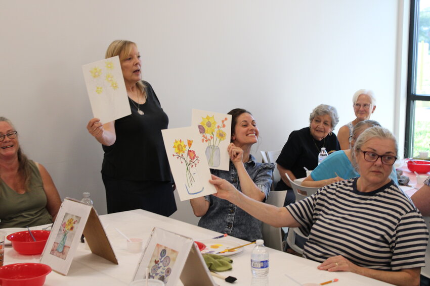 Instructor Carol Peper, Shannon Gardner and Brigitte Gardner hold up their watercolor paintings for everyone in the room to see. Peper wanted the painters to show off their work so everyone could see just how different each design was.