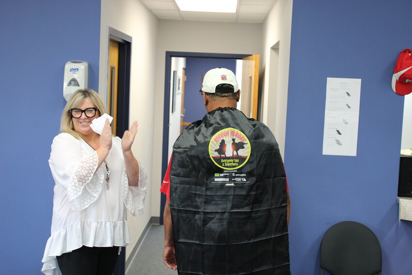 Warren County Record Sales Manager Kelley Wright applauds as Alfred Wheeler shows off his new Hidden Hero superhero cape.