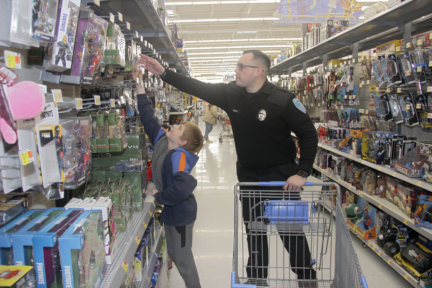 A LITTLE HELP &mdash; Officer J. Malta helps Marcus, 9, grab a Beyblade toy from a high hanger while the two were shopping together at Walmart Saturday during Truesdale&rsquo;s Shop With A Cop program. Eight children from three families got to go on a shopping trip.