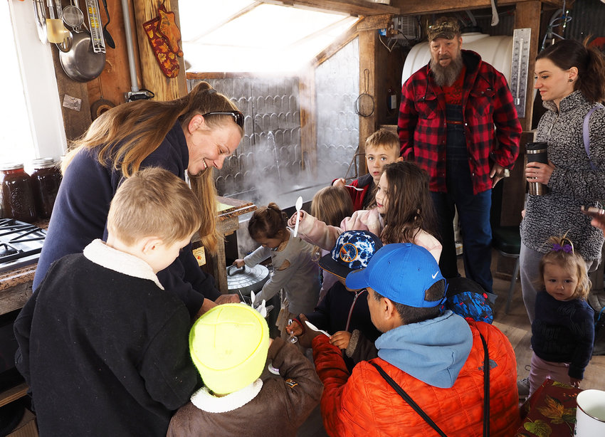 JUST A TASTE &mdash; Visiting homeschool students enjoy the taste of fresh maple syrup served by Cheryl Vieth, left, at Vieth Valley Farms in Marthasville. Tim Vieth, center, monitors maple sap being cooked in a 25-gallon stainless steel pan in the couple&rsquo;s maple syrup shack, built specially for the process.