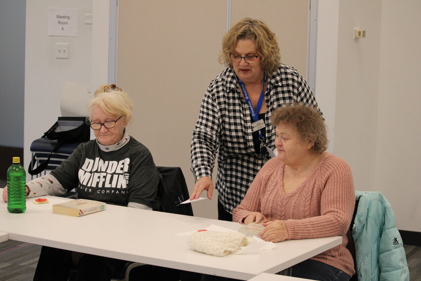 Robin Schaefferkoetter, the branch manager at the Warrenton Scenic Regional Library, hands out discussion questions to participants in the Literary Travelers book club during the group&rsquo;s meeting on Dec. 27.