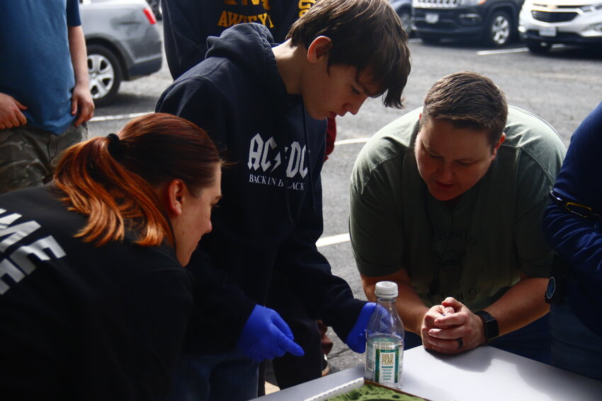 Pictured, Devin, a student at High Road School works to pull fingerprints from a plastic bottle with help from Lesch, right, and teacher Kristi Hoffman, left.