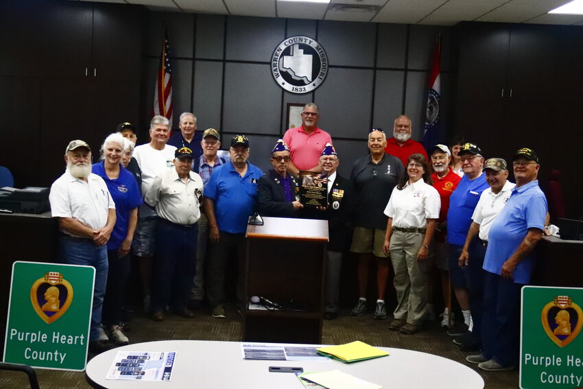 Following the Commissioners proclamation, attendees gathered for a photo with the plaque and the new Purple Heart County signs.