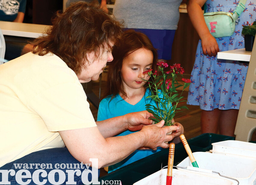 Master Gardener Becky Kemper shows Samantha Evans how to replant her flower as they prepare it for repotting.