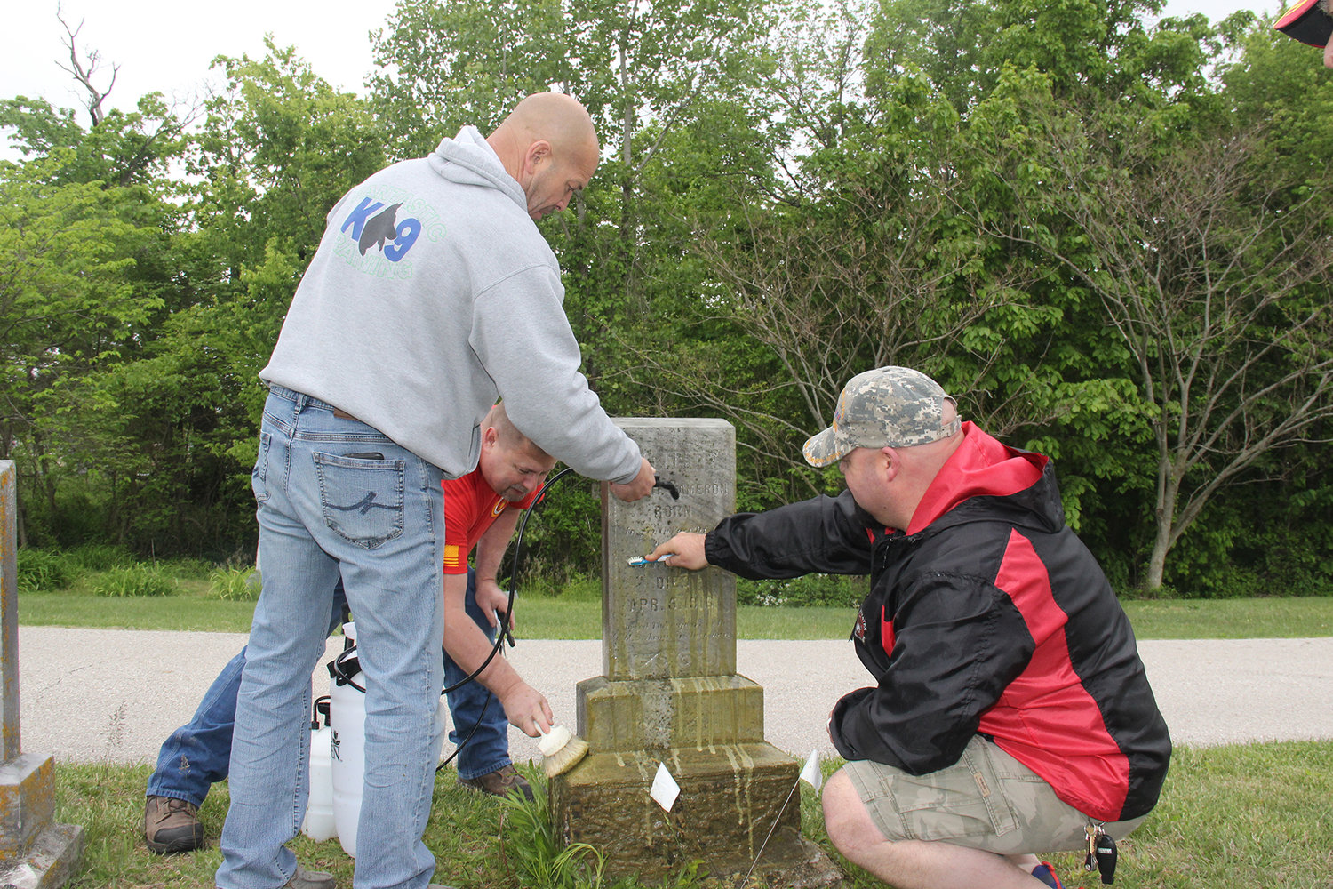 Warrenton Marine Corps League members Mike Weicht, Erick Rasche and Ryan Petras work together to clean the headstone of a 19th-century veteran buried at the Warrenton City Cemetery on Saturday, May 15. Green lichen and grime can be seen getting washed away with the help of a special chemical.