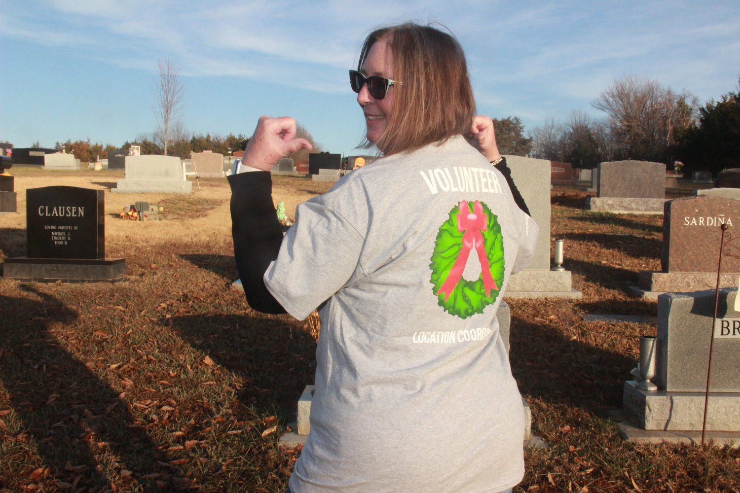 DEDICATED VOLUNTER — Andrea Romaker demonstrates the volunteer shirt given to those who help with the Wreaths Across America initiative. Romaker is the local coordinator who arranges for the memorial effort to be brought to the Warrenton City Cemetery and Holy Rosary Cemetery.