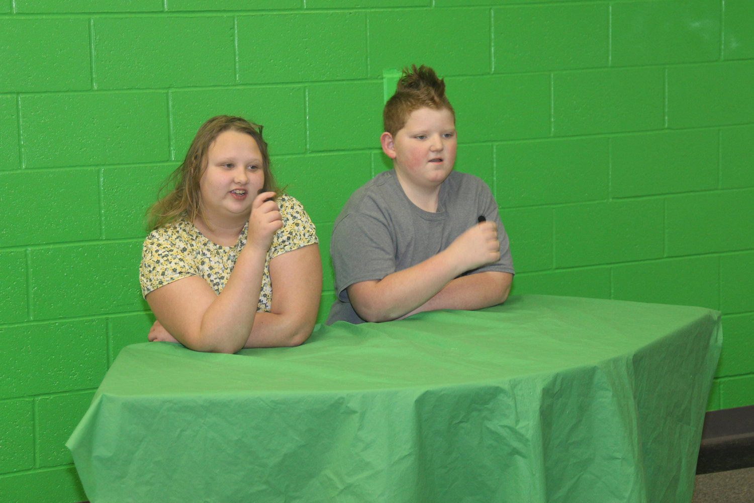 SCHOOL NEWS — Fifth graders Jolenne Barnes and Sam Williams serve as anchors for recorded news announcements at Rebecca Boone Elementary. Other students provide their scripts and add backgrounds to their green screen environment through video editing.